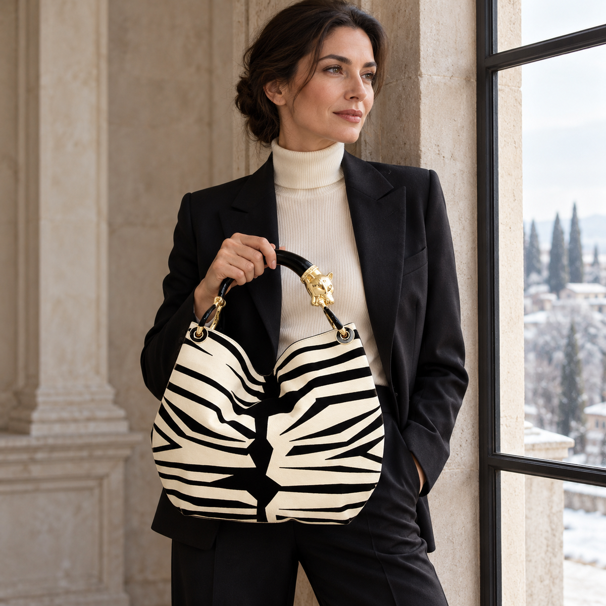 Woman in a black suit holding the ivory and black zebra-print panther-handle bag beside a window.