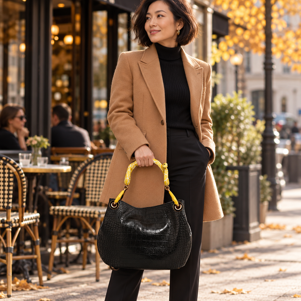 Woman carrying the INGA black croco-embossed leather medium handbag with yellow snake sculpture handle, styled for autumn.